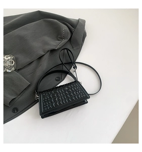 Detail of black glossy handbag featuring textured geometric embossed flap and shoulder strap