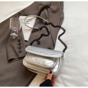 Detail of silver chevron quilted crossbody bag with black chain strap on white fabric