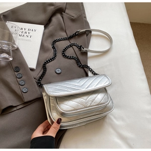 Detail of silver quilted V-pattern flap bag with black chain strap on a dark blazer