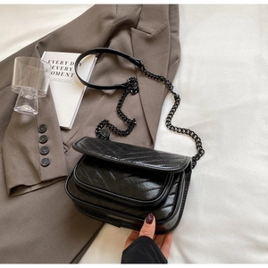 Detail of black quilted crossbody bag with matte chain strap on a brown blazer fabric