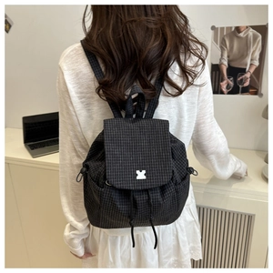Detail of black checkered backpack featuring side drawstrings and puzzle buckle closure