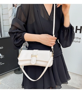 Detail of white leather baguette bag with gold buckle on a model in a street style setting