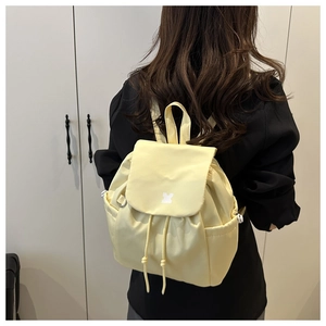 Detail of light yellow drawstring backpack showing side pockets and metal buckles