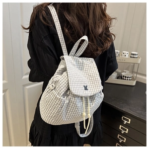 Rear view of a person wearing a white and grey plaid drawstring backpack in a cafe