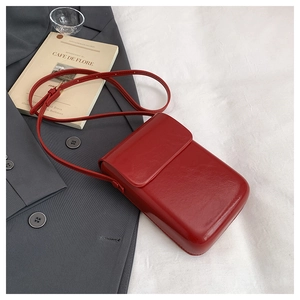 Detail view of a red glossy minimalist square crossbody phone bag on a grey blazer suit