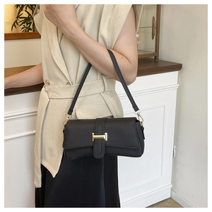 Close-up of black leather baguette bag with gold H-shaped buckle on a model