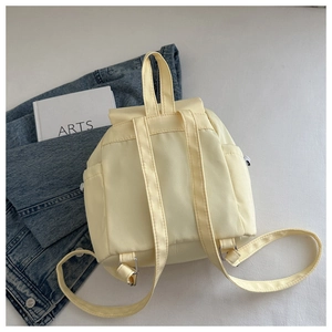 Detailansicht des cremegelben Rucksacks mit verstellbaren Trägern und Seitentaschen auf Denim