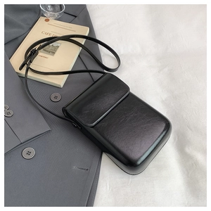 Close-up of a black minimalist square crossbody bag with a sleek flap and leather texture