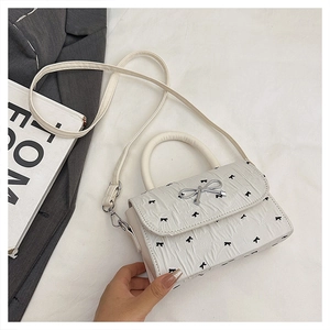 Close-up of white pleated mini bag with silver metal bow and black butterfly prints