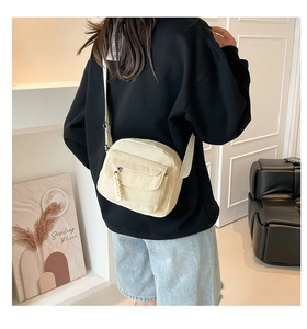Detail of off-white corduroy crossbody bag with adjustable strap and textured front pocket