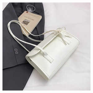 Close-up of a white rectangular handbag with a delicate bow on the slim shoulder strap