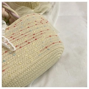 Detailed texture of woven straw tote bag featuring colorful dots and white lace ribbon decoration