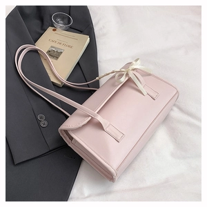 Detail of pink faux leather shoulder bag featuring a stylish cream ribbon bow decoration