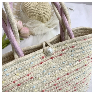 Detail of straw woven tote bag featuring colorful pom-poms and a large pearl clasp