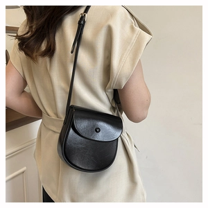 Detail view of a matte black leather saddle bag worn by a model in a beige sleeveless top