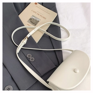 Detailed view of cream saddle crossbody bag on a gray suit with vintage book backdrop