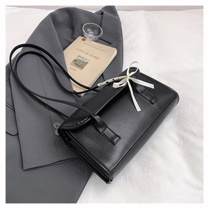 Detail of black leather underarm bag featuring a stylish white ribbon bow on a grey blazer