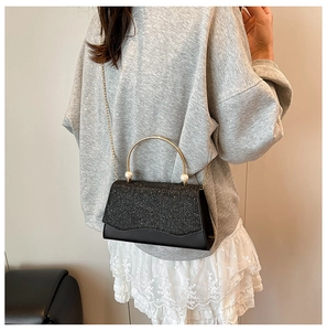 Sac à main noir à paillettes avec poignée en perles et chaîne dorée porté par mannequin