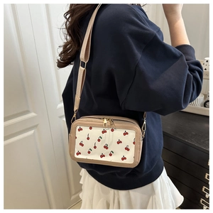 White crossbody bag with cherry prints and dual zippers worn by a model in casual attire