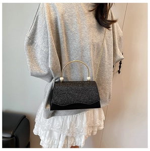 Détail d'un sac à main noir pailleté avec poignée anneau doré et perles blanches