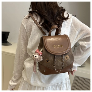 Détail d'un mini sac à dos en cuir marron avec broderie dorée et charm d'ours en peluche