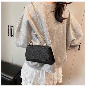 Détail du sac à main en paillettes noires avec poignée dorée, perles et chaîne en métal