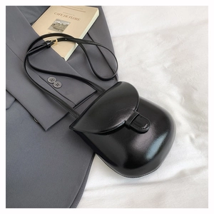 Close-up of minimalist black shiny crossbody bag on a grey blazer with adjustable strap