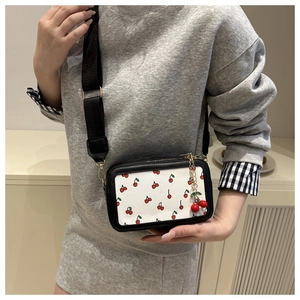 Detailed view of the small square crossbody bag with red cherry prints and wide strap