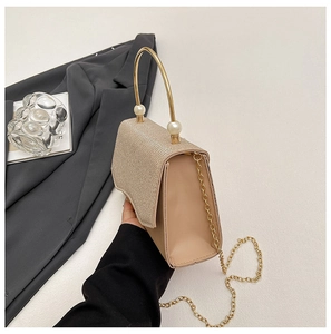 Détail d'une pochette dorée champagne avec rabat à paillettes et poignée en perle