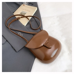 Close-up of a glossy dark brown leather crossbody bag with adjustable strap and buckle