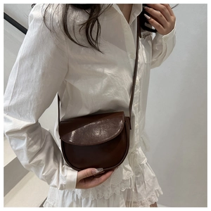 Detail of a vintage dark brown leather saddle bag styled on a model's shoulder
