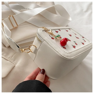Detalle de bolso bandolera blanco con estampado de cerezas y colgante de cereza en cremallera