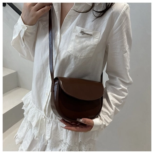Detail shot of brown glossy patent leather saddle bag with smooth finish and stitching