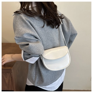 Close-up of white saddle bag worn on shoulder over a casual grey sweatshirt and shirt