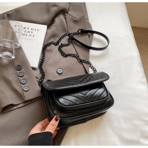 Detail of black chevron quilted crossbody bag with metal chain strap on textured blazer