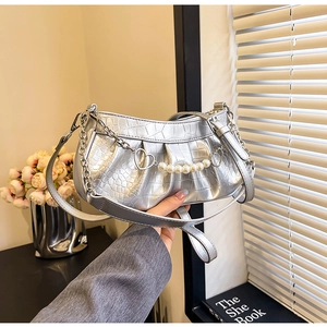 Détail d'un sac argenté plissé avec motif crocodile et chaîne ornée de perles élégantes
