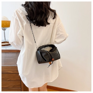 Détail d'un sac bandoulière plissé noir avec chaîne tressée et perles d'ambre décoratives