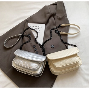 Detail of silver and cream V-quilted handbags with black chain straps on brown blazer