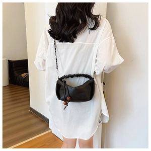 Détail du sac plissé noir avec bandoulière en chaîne et perles en bois ornementales chic