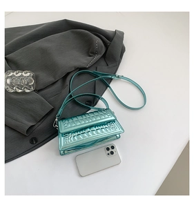 Detail view of teal croc-embossed glossy bag shown with smartphone for size scale