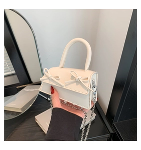 Close-up of a mini cream white handbag featuring dual bows and a silver metal chain