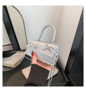 Close-up of silver mini handbag with metallic finish and bow details on a table