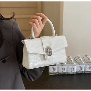 Detail of white crocodile pattern handbag with silver oval metal lock and top handle