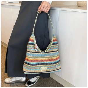 Close-up of a colorful striped woven tote bag with green strap and bead charm detail