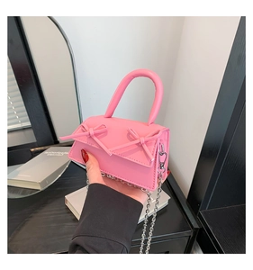 Close-up of a mini pink crossbody bag featuring dual bows and silver chain strap