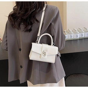 Detail of white crocodile pattern flap bag with silver oval twist lock and handle