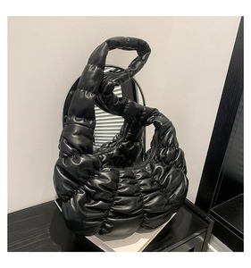 Detail of black pleated croissant bag with glossy quilted texture and cloud-like design