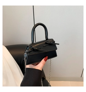 Detail of mini black square bag featuring elegant twin bow accents and a silver chain strap