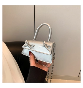 Detail of silver mini handbag with bows and metal chain strap held by a hand