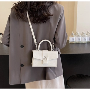 Detail shot of the white crocodile-embossed mini bag with a metallic oval turn-lock closure